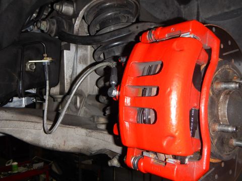 2003 Ford Crown Victoria - red painted brake caliper with a braided stainless brake line beside a coil spring and exposed wheel hub.
