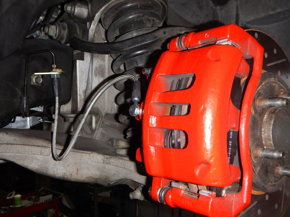 Red painted brake caliper with braided line, coil spring and wheel hub