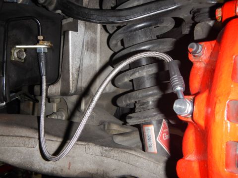 2003 Ford Crown Victoria - braided stainless-steel brake line routed past a coil spring and proportioning fitting to a red brake caliper.