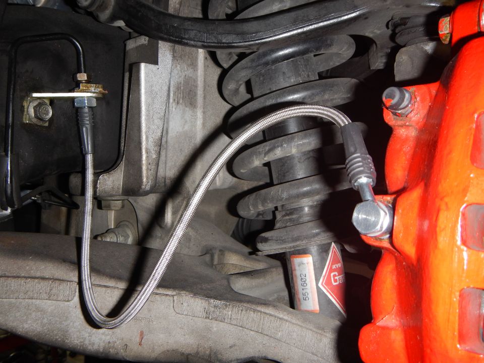 Braided brake line routed along coil spring to a red caliper, underbody