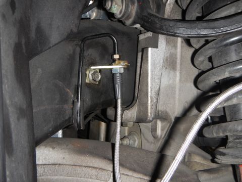 2003 Ford Crown Victoria - underbody close-up of a brake hard-line bracket and fitting joining a braided hose near the coil spring.