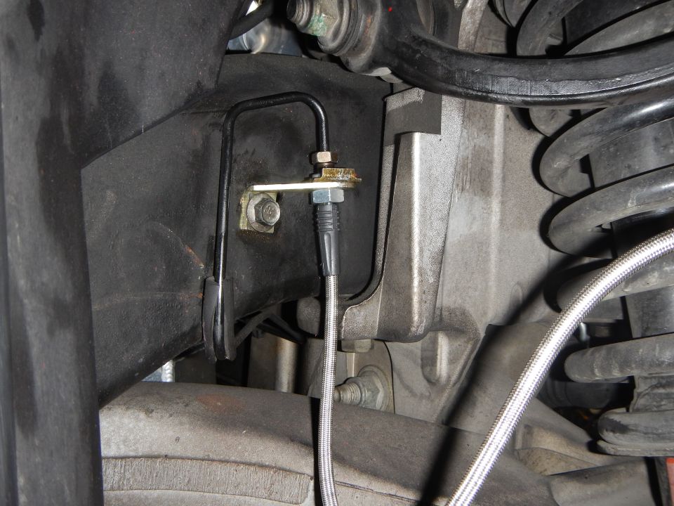 Brake line bracket and fitting with braided hose near coil spring underbody