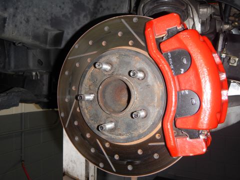 2003 Ford Crown Victoria - underbody view of a cross-drilled, slotted brake rotor with a red caliper gripping it beside the wheel hub.