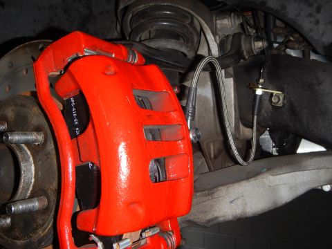 2003 Ford Crown Victoria - Photo of a red-painted front brake caliper over a vented rotor with a stainless braided brake hose.