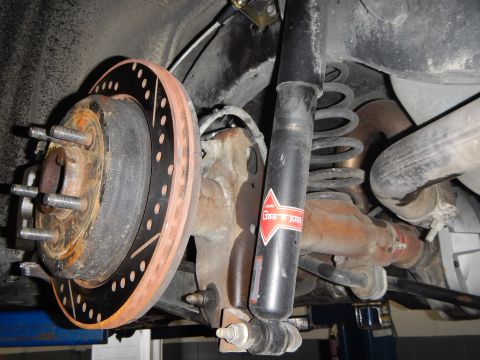 2003 Ford Crown Victoria - Photo of a rear brake rotor, hub and shock absorber with coil spring on a shop lift.