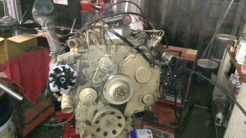 1996 Ford Bronco - A diesel engine, likely from a 1996 Ford Bronco, is mounted on a stand in a workshop. The engine features an alternator, various pulleys, a…