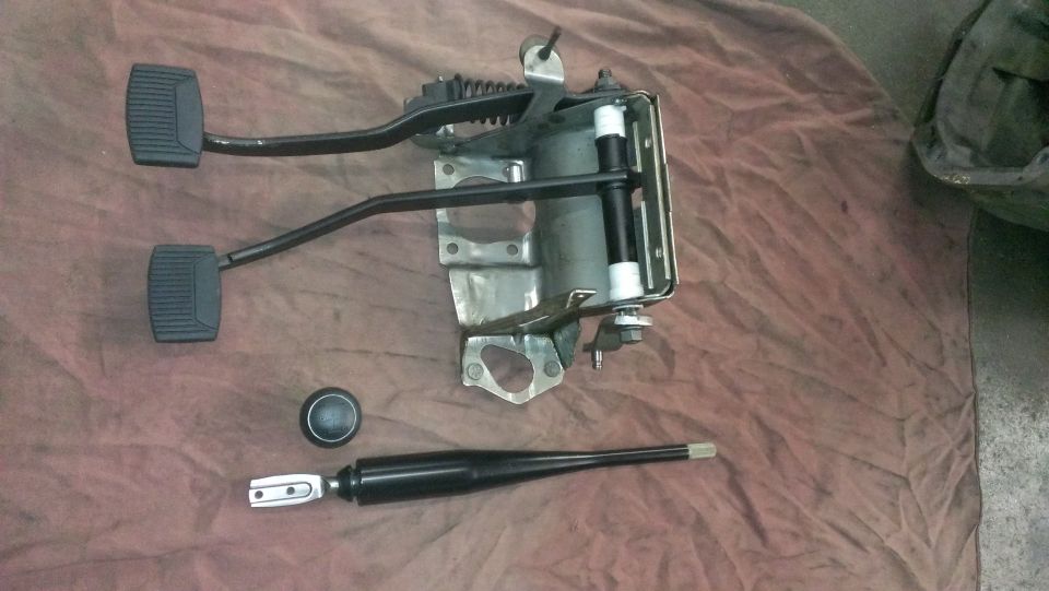 Clutch pedal assembly, brake pedal, shift knob, and shifter lever on a brown cloth.