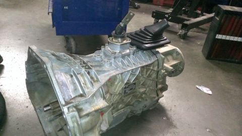 1996 Ford Bronco - A manual transmission with a shifter and rubber boot is shown lying on a concrete floor. The transmission housing is made of aluminum and a…