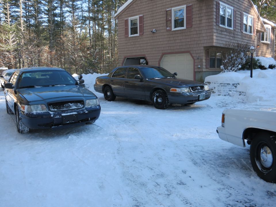 Several sedans parked in a snowy driveway in front of a house