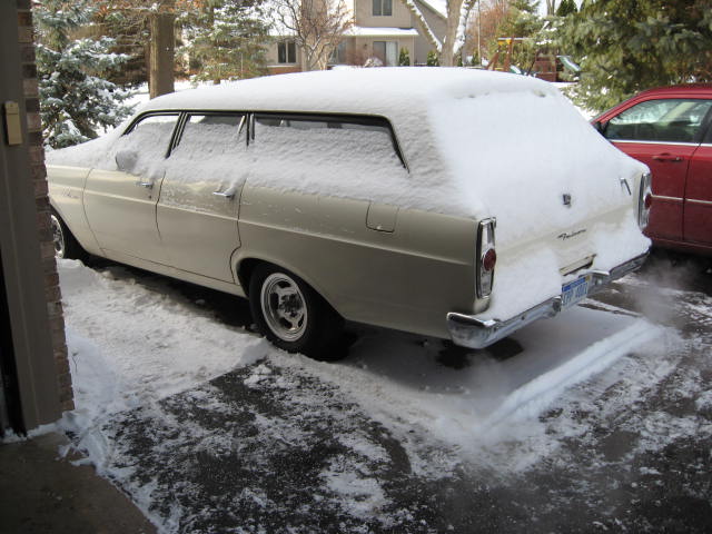 Snow-covered beige station wagon parked on a snowy driveway.