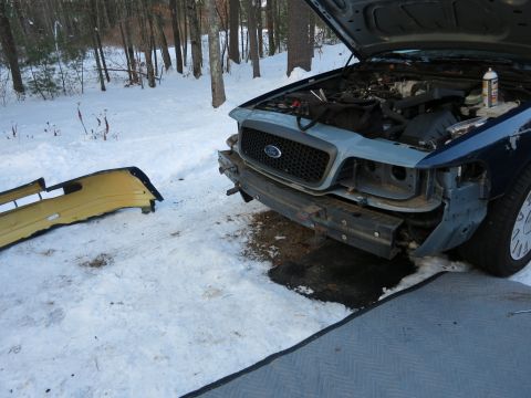 2001 Ford Crown Victoria - Photograph of a Ford Crown Victoria mid-repair with a yellow bumper cover on the snow, not a technical document.