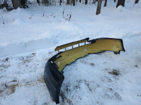 2001 Ford Crown Victoria - Photograph of a yellow and black front bumper cover lying on the snow, not a technical document.