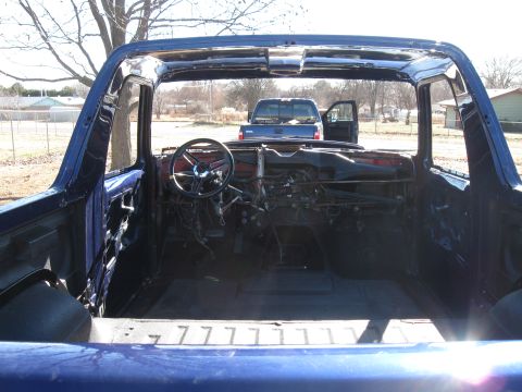 1982 Ford Bronco - The interior of a blue Ford Bronco is shown with the doors removed, revealing the dashboard, steering wheel, and exposed wiring. A blue pic…