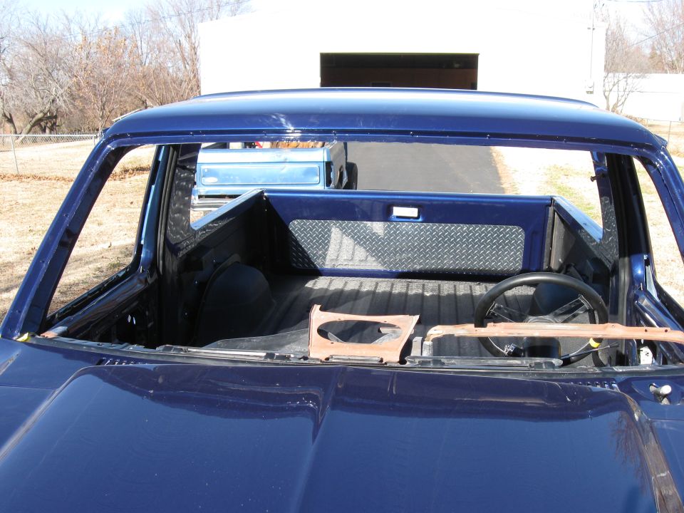 Interior of a dark blue pickup truck with windshield removed, showing steering wheel.
