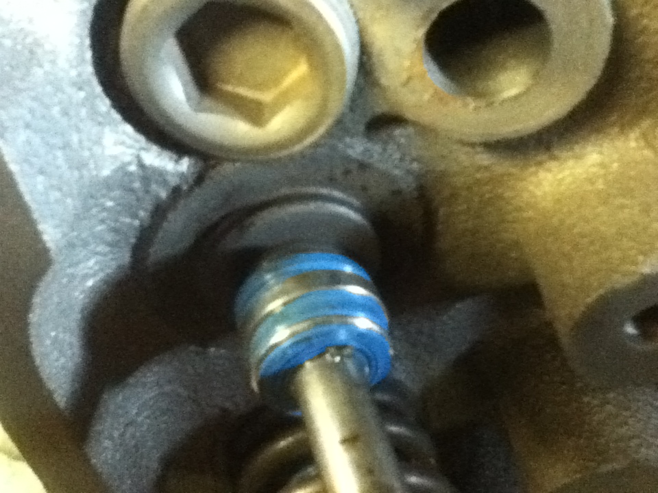 Close-up of a valve stem seal with blue bands on a metal rod, part of an engine