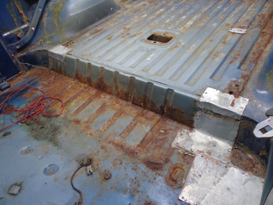Interior floor of a heavily rusted vehicle with patches of new metal and red wiring