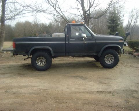 1985 Ford F-150 - A black pickup truck is parked outdoors on a dirt surface with trees in the background.