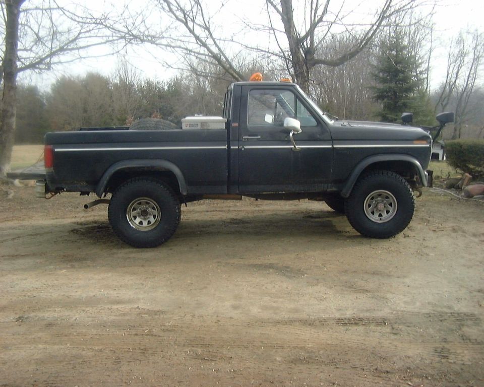 Black lifted Ford F-150 regular cab pickup in side view on dirt lot.