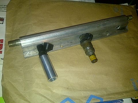 1995 Ford Probe - A fuel rail with two fuel injectors is mounted on a piece of aluminum extrusion. The assembly is resting on a brown paper surface.