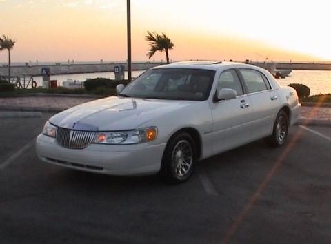2002 Lincoln Town Car - A white 2002 Lincoln Town Car is parked near a waterfront during sunset.