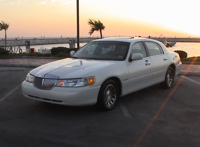 White Lincoln Town Car sedan at a waterfront parking lot at sunset, 3/4 front view