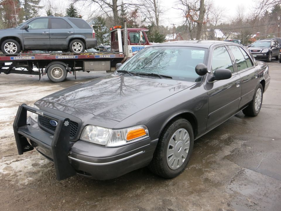 Front three-quarter view of gray Ford Crown Victoria with push bar near a tow truck