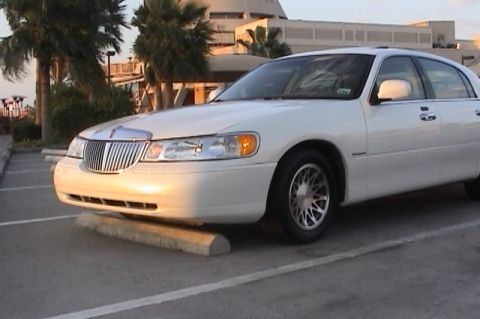 2002 Lincoln Town Car - A white 2002 Lincoln Town Car is seen from a three-quarter front view, parked in a lot with palm trees and a building in the background.