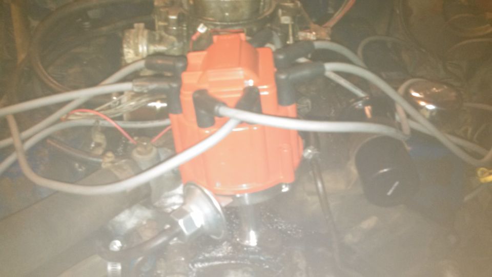 Orange HEI distributor cap with spark plug wires in a vehicle engine bay.