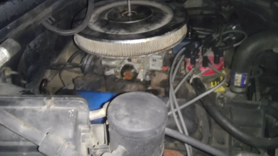 Close-up of a V8 engine bay with air cleaner, distributor, and hoses visible.