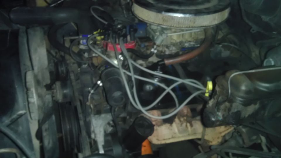 Close-up of a V8 engine bay with distributor, wires, air filter, and fan.
