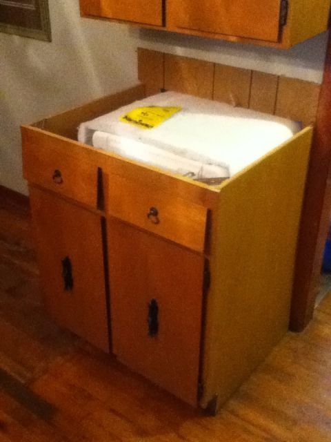 2006 Ford E350 - A wooden cabinet with two drawers and two cabinet doors is shown. A white object with a yellow label is inside the cabinet.