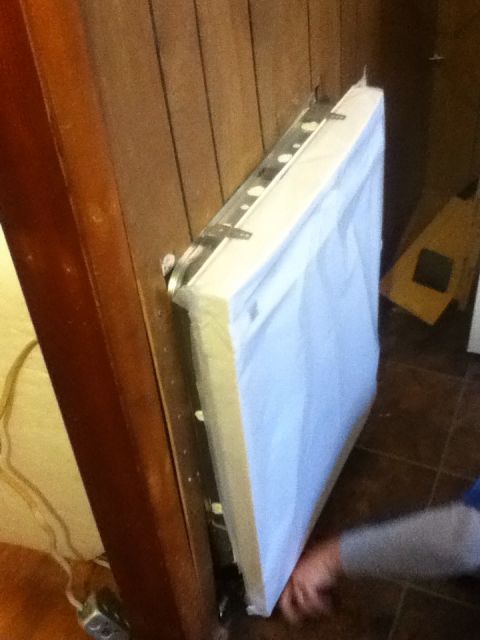 2006 Ford E350 - A white mattress is leaning against a wooden wall, attached by metal brackets. A person's arm is visible reaching towards the bottom of the…