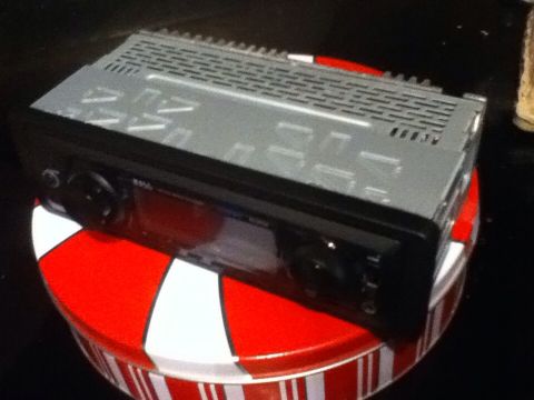 2006 Ford E350 - A car stereo head unit is shown resting on a red and white striped tin. The head unit is black with a silver top and has a digital display…