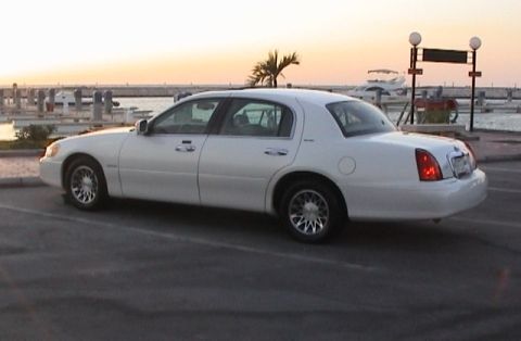 2002 Lincoln Town Car - A white 2002 Lincoln Town Car is seen from the side near a marina with boats in the background.