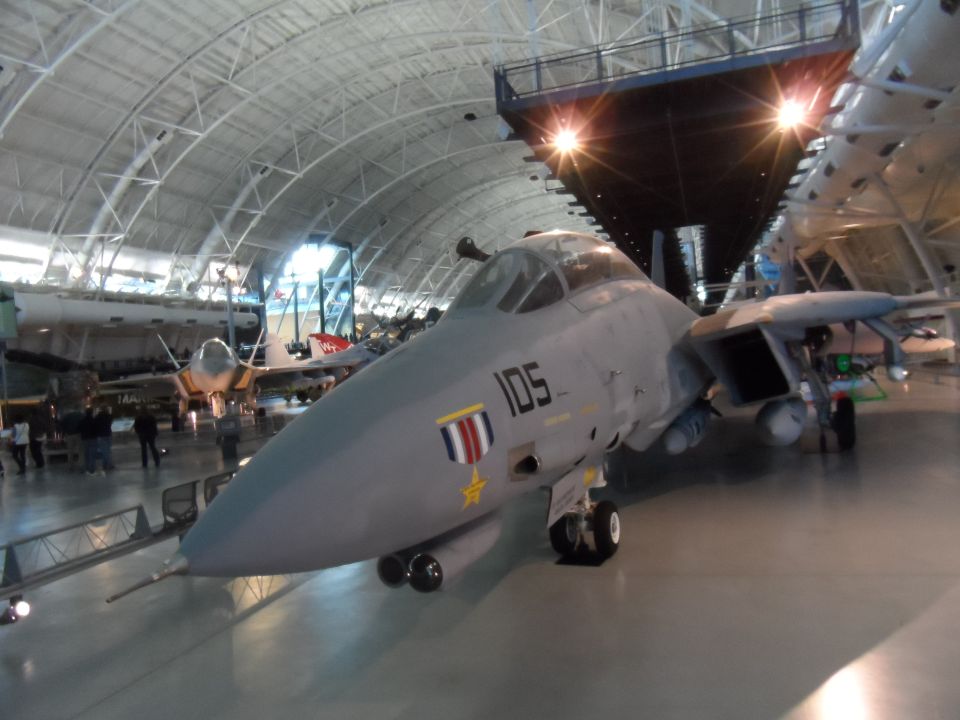 Gray Grumman F-14 Tomcat fighter jet with number 105 on the side, indoors.