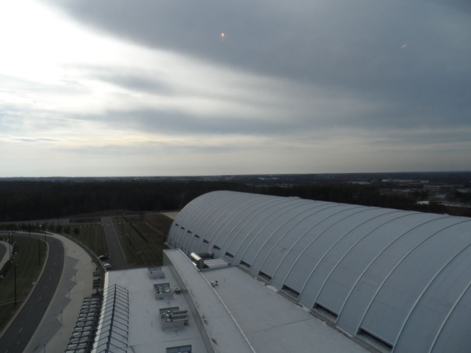 Large arched building with a cloudy sky overhead and a road curving away
