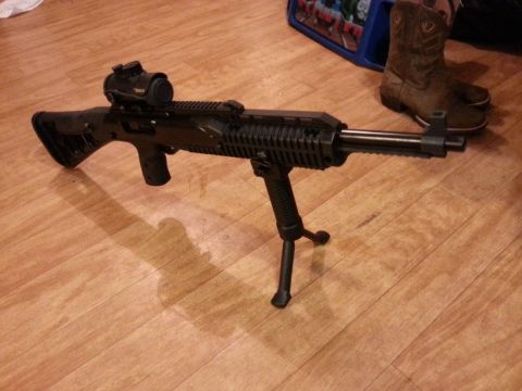 1995 Ford F-150 - A rifle equipped with a bipod and red dot sight rests on a hardwood floor, with cowboy boots and a toy bin visible in the background.