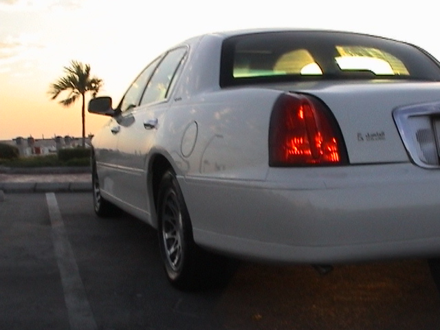 Low close 3/4 rear of white Lincoln Town Car taillamp and quarter panel at sunset