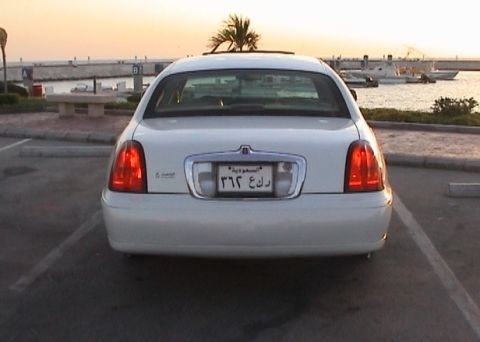 2002 Lincoln Town Car - A white Lincoln Town Car is parked near a harbor with boats in the background during sunset.