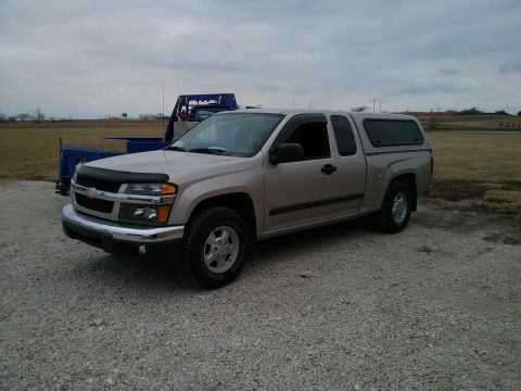 1986 Ford Bronco - A tan Chevrolet Colorado pickup truck is parked on a gravel lot under a cloudy sky.