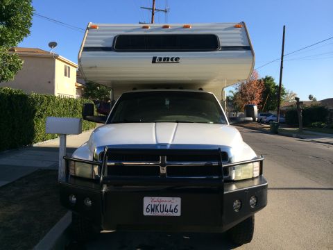 1997 Dodge 3500 - A white Dodge Ram pickup truck with a Lance camper shell is parked on a residential street.