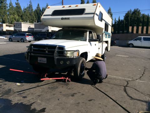 1997 Dodge 3500 - A person works on the front tire of a white pickup truck fitted with a Lance camper shell.