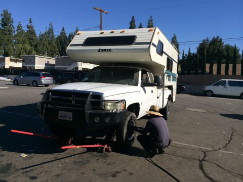 1997 Dodge 3500 - Person working on front tire of a white 1997 Dodge Ram pickup with a Lance camper shell.