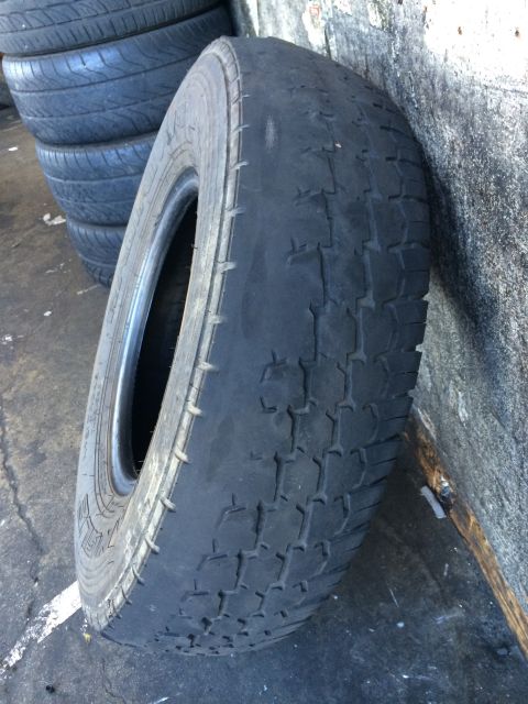 1997 Dodge 3500 - A heavily worn tire is shown leaning against a textured wall, with other tires stacked in the background.
