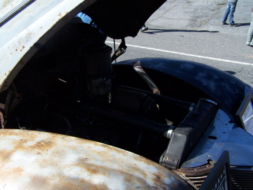 Rusty hood open on a dark vehicle, revealing a dark engine bay with a radiator