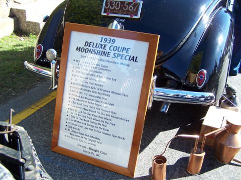 1971 Ford Ranchero - A sign details the custom build of a 1939 Deluxe Coupe Moonshine Special, parked outdoors.