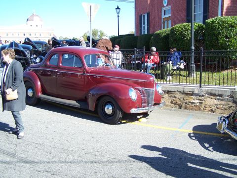 1971 Ford Ranchero - A maroon 1940 Ford Coupe is parked on a street, with other vehicles and spectators present.