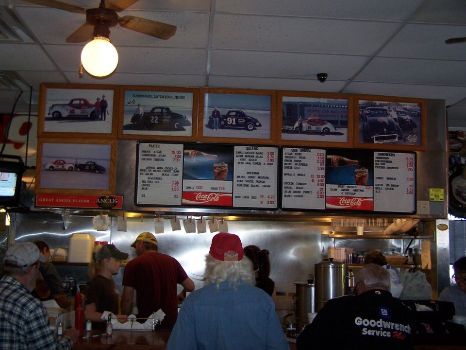 Diner interior with framed photos of race cars on the wall above menu boards