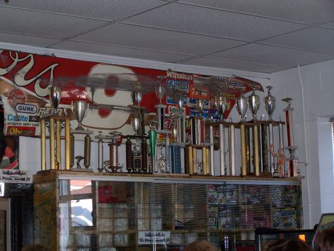 1971 Ford Ranchero - A collection of trophies and racing memorabilia is displayed on shelves.