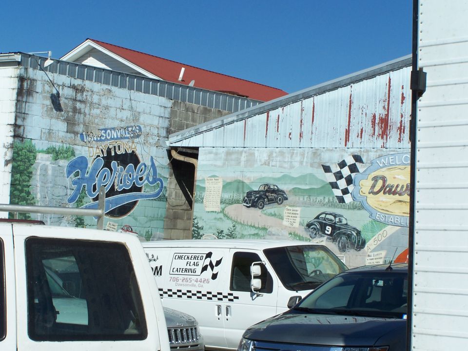 Mural on a building wall depicting race cars on a track, with text 'DAYTONA Heroes' and 'WELCOME Dawsonville'
